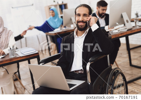 A man sits in a wheelchair with a laptop. A man sits in a wheelchair with a laptop. 70167191