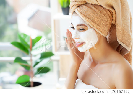 Close-up portrait of beautiful girl with a towel on her head applying facial mask Close-up portrait of beautiful girl with a towel on her head applying facial mask 70167192