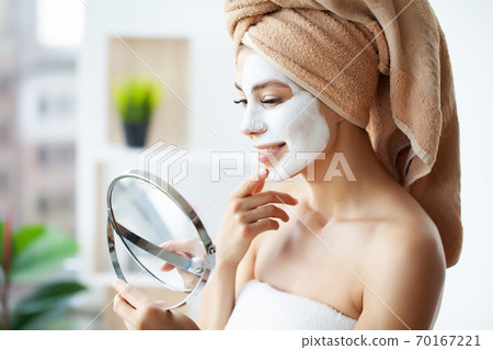 Close-up portrait of beautiful girl with a towel on her head applying facial mask 70167221