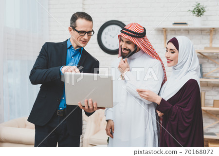 A man shows Arab couple something on a notebook. 70168072