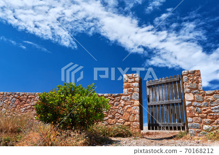 Countryside landscape. Rustic stone wall fence and aged black timber wicket door. Great blue sky with awesome clouds. 70168212