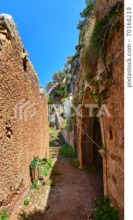Walkway in ruins of remote abandoned Katholiko monastery in Avlaki gorge of Akrotiri peninsula, Chania, Crete, Greece. Wild spring foliage, clay walls 70168219