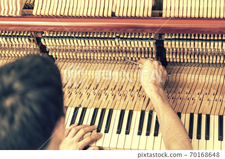 Piano tuning process. closeup of hand and tools of tuner working on grand piano. Detailed view of Upright Piano during a tuning. toned 70168648