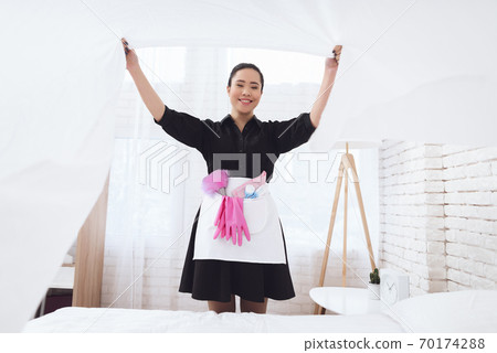 Asian housekeeper in special uniform covers bed. Asian housekeeper in special uniform covers bed. 70174288