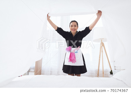 Asian housekeeper makes a bed and rejoices. 70174367