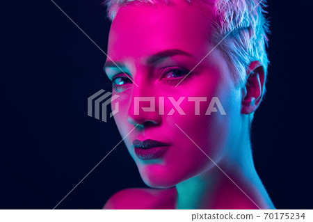 Portrait of female fashion model in neon light on dark studio background. 70175234