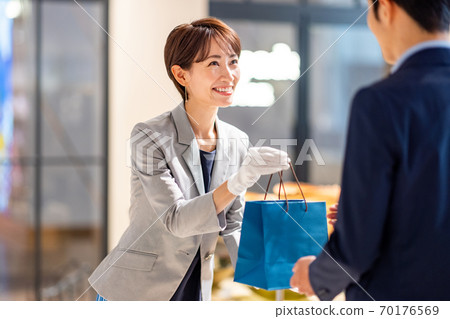 Female clerk handing over a paper bag Photo cooperation: g GIFT AND LIFE STYLE Female clerk handing over a paper bag Photo cooperation: g GIFT AND LIFE STYLE 70176569