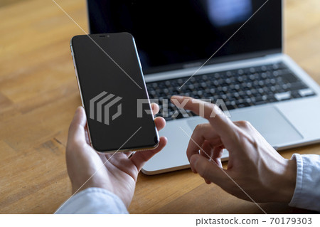 Man with smartphone in front of laptop 70179303