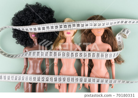 Dolls wrapped in measuring tape. Unrecognizable fashion dolls, weight loss concept. Fasting, weightloss and slimming. Diet, anorexia, eating disorder, overeating control, fight for perfect fit body. Dolls wrapped in measuring tape. Unrecognizable fashion dolls, weight loss concept. Fasting, weightloss and slimming. Diet, anorexia, eating disorder, overeating control, fight for perfect fit body. 70180331