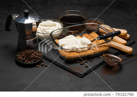tiramisu dessert cooking - Traditional Italian Savoiardi ladyfingers Biscuits and cream in glass baking dish, coffe maker on dark concrete background tiramisu dessert cooking - Traditional Italian Savoiardi ladyfingers Biscuits and cream in glass baking dish, coffe maker on dark concrete background 70182786