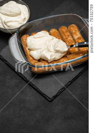 tiramisu dessert cooking - Traditional Italian Savoiardi ladyfingers Biscuits and cream in glass baking dish on dark concrete background tiramisu dessert cooking - Traditional Italian Savoiardi ladyfingers Biscuits and cream in glass baking dish on dark concrete background 70182789