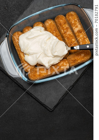 tiramisu dessert cooking - Traditional Italian Savoiardi ladyfingers Biscuits and cream in glass baking dish on dark concrete background 70182791
