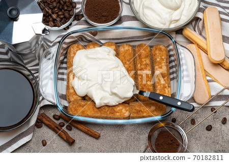 tiramisu dessert cooking - Traditional Italian Savoiardi ladyfingers Biscuits and cream in glass baking dish, coffe maker on concrete background 70182811