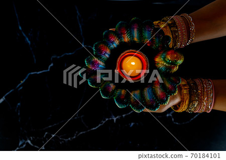 Happy Diwali - Woman hands with henna holding lit candle isolated on dark background. Happy Diwali - Woman hands with henna holding lit candle isolated on dark background. 70184101