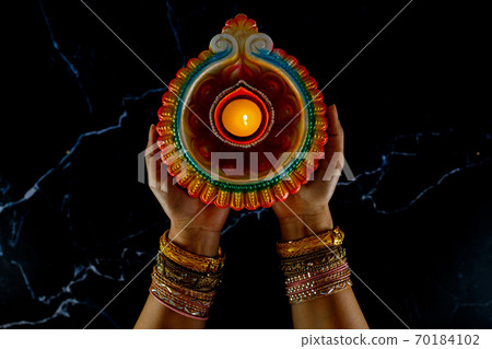 Happy Diwali - Woman hands with henna holding lit candle isolated on dark background. Happy Diwali - Woman hands with henna holding lit candle isolated on dark background. 70184102