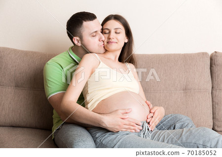A young couple is expecting a baby. husband hugs the belly of his pregnant wife at home A young couple is expecting a baby. husband hugs the belly of his pregnant wife at home 70185052