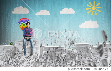 Young man sitting on pile of paper documents. 70185573