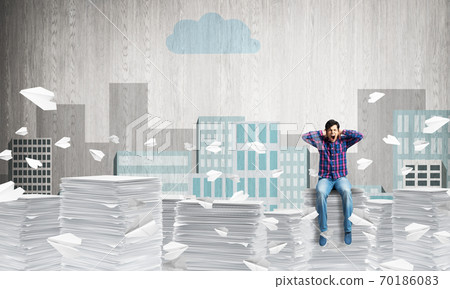 Young man sitting on pile of paper documents. Young man sitting on pile of paper documents. 70186083