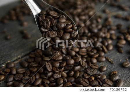 Fresh roasted arabica coffee beans in a metal spoon and scattered coffee beans on a wooden table. Fresh roasted arabica coffee beans in a metal spoon and scattered coffee beans on a wooden table. 70186752