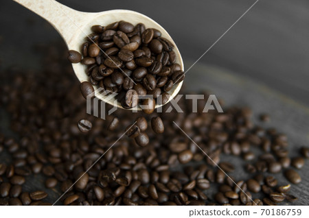 Fresh roasted arabica coffee beans falling from a oaken spoon on a wooden table. Fresh roasted arabica coffee beans falling from a oaken spoon on a wooden table. 70186759