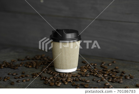 Paper cup of coffee with roasted coffee beans on wooden table background. Mug of black coffee. 70186783