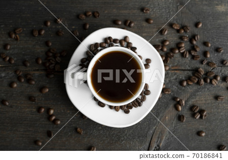 Coffee cup with roasted coffee beans on wooden table background. Mug of black coffe with scattered coffee beans on a wooden table. Fresh coffee beans. Coffee cup with roasted coffee beans on wooden table background. Mug of black coffe with scattered coffee beans on a wooden table. Fresh coffee beans. 70186841