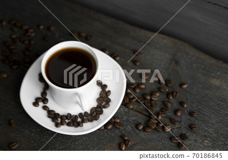 Coffee cup with roasted coffee beans on wooden table background. Mug of black coffe with scattered coffee beans on a wooden table. Fresh coffee beans. Coffee cup with roasted coffee beans on wooden table background. Mug of black coffe with scattered coffee beans on a wooden table. Fresh coffee beans. 70186845