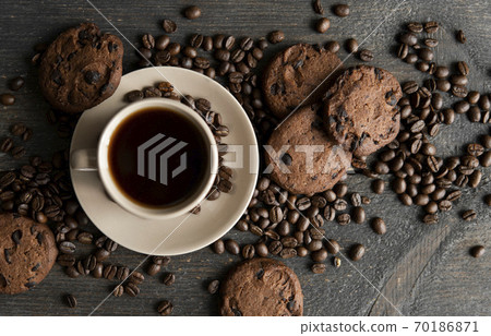Coffee cup with cookies on wooden table background. Mug of black coffee with scattered coffee beans and cookies on a wooden table. Fresh coffee beans. Coffee cup with cookies on wooden table background. Mug of black coffee with scattered coffee beans and cookies on a wooden table. Fresh coffee beans. 70186871