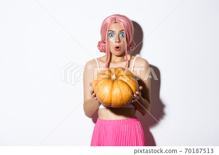Image of attractive girl in pink wig looking surprised while holding pumpkin for halloween party, standing over white background Image of attractive girl in pink wig looking surprised while holding pumpkin for halloween party, standing over white background 70187513