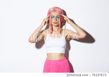 Portrait of distressed caucasian girl with pink wig and party makeup, standing with closed eyes and touching head, trying to think or remember something Portrait of distressed caucasian girl with pink wig and party makeup, standing with closed eyes and touching head, trying to think or remember something 70187673