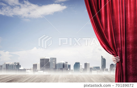 Business city in gray fog behind red curtain and hand holding it Business city in gray fog behind red curtain and hand holding it 70189072