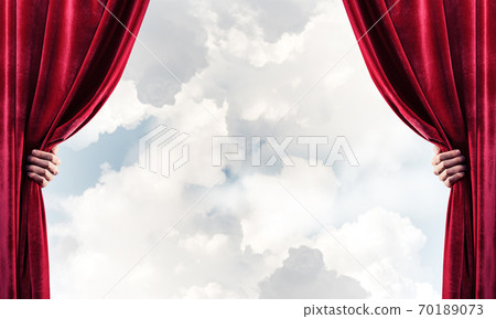 Cloudy landscape behind red curtain and hand holding it Cloudy landscape behind red curtain and hand holding it 70189073