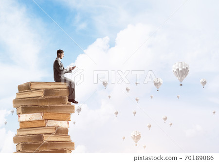 Man businessman on stack reading book and aerostats flying around Man businessman on stack reading book and aerostats flying around 70189086