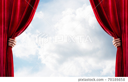 Cloudy landscape behind red curtain and hand holding it 70189858