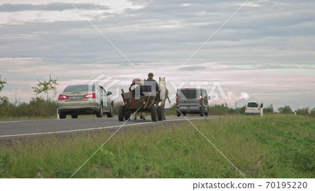 on the new road after repair peasants go on fires and horses, old transport, poor people on transport are overtaken by modern cars, people out of modern civilization on the new road after repair peasants go on fires and horses, old transport, poor people on transport are overtaken by modern cars, people out of modern civilization 70195220