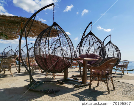 Outdoor terrace with Empty wooden table and chair with Sea view. Hanging chairs, table at the terrace, umbrella from the sun. Outdoor terrace with Empty wooden table and chair with Sea view. Hanging chairs, table at the terrace, umbrella from the sun. 70196867