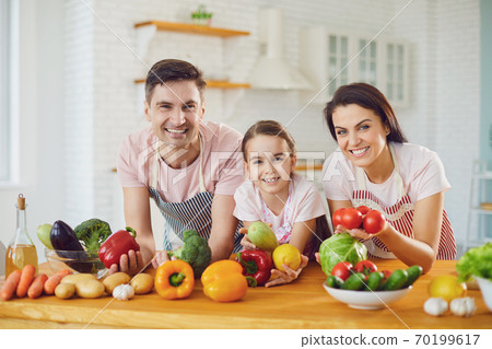 Happy family smiling at a table with fresh vegetables make salad in the kitchen. Happy family smiling at a table with fresh vegetables make salad in the kitchen. 70199617