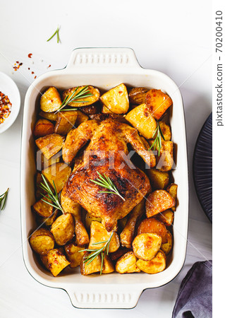 Baked whole chicken with potatoes and rosemary in black dish, white background, top view. 70200410
