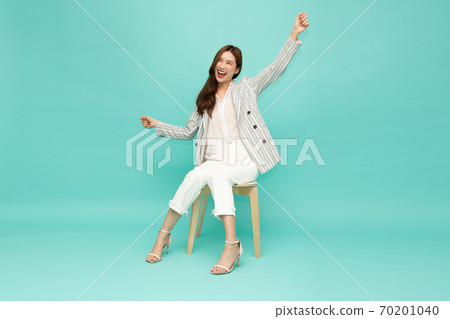 Attractive beautiful Asian woman sitting on white modern chair and hands up on green background. Attractive beautiful Asian woman sitting on white modern chair and hands up on green background. 70201040