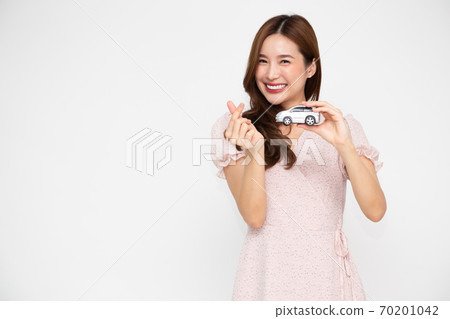 Young Asian woman holding car model and showing mini heart sign isolated on white background. 70201042
