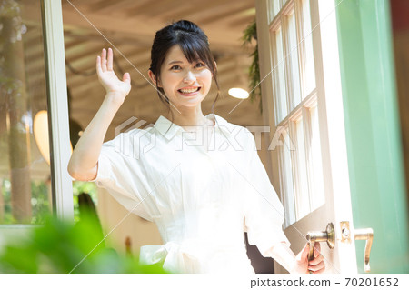 Young woman waving at the front door 70201652