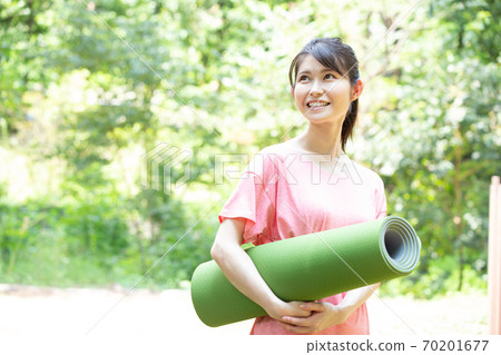 A woman holding a yoga mat in a fresh green park Photographing cooperation: Santome Konjyamura 70201677