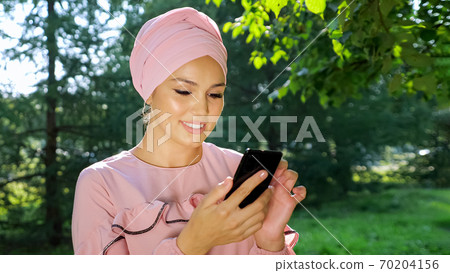 Beautiful muslim woman in turban with phone on background of trees Beautiful muslim woman in turban with phone on background of trees 70204156