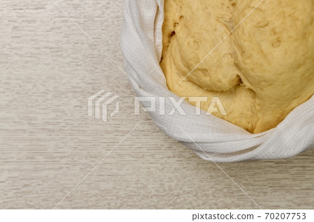 The puffed yeast dough has risen in a bowl. Tied around with a braided white waffle towel. The puffed yeast dough has risen in a bowl. Tied around with a braided white waffle towel. 70207753