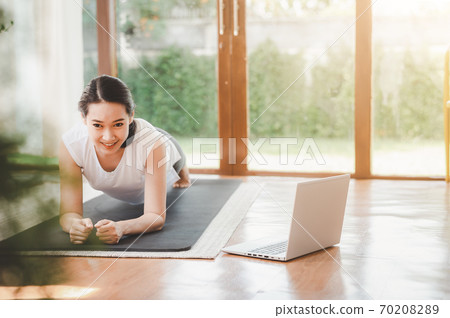 woman doing plank exercise at home while watching online workout session from laptop 70208289