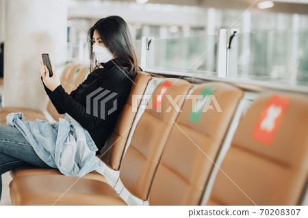 woman traveler wearing mask sitting on social distancing chair using smartphone during coronavirus woman traveler wearing mask sitting on social distancing chair using smartphone during coronavirus 70208307