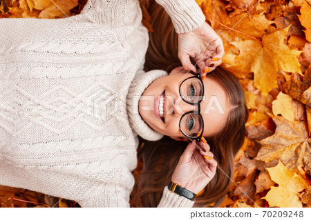 Young model of a happy woman lies in orange leaves Young model of a happy woman lies in orange leaves 70209248