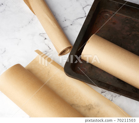 metal pan and rolls of brown parchment paper on a white table metal pan and rolls of brown parchment paper on a white table 70211503
