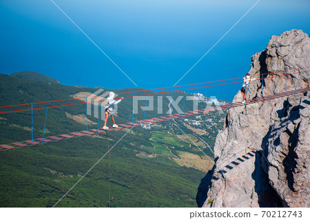 Girls crossing the chasm on the rope bridge. Black sea background, Crimea, Russia Girls crossing the chasm on the rope bridge. Black sea background, Crimea, Russia 70212743