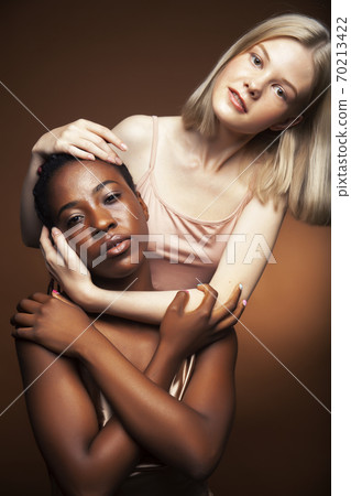 two pretty girls african and caucasian blond posing cheerful together on brown background, etnithity diverse lifestyle people concept two pretty girls african and caucasian blond posing cheerful together on brown background, etnithity diverse lifestyle people concept 70213422